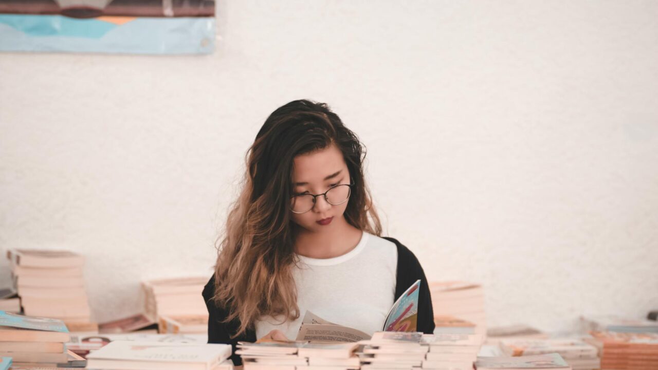 photo of woman reading book in room full of books