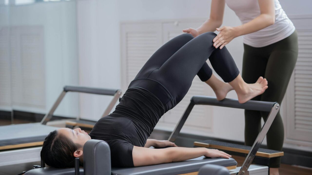 fitness instructor assisting woman doing pilates